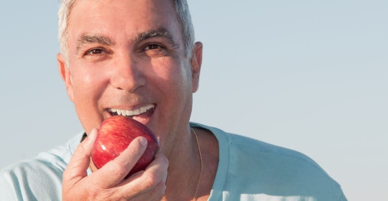 older man with dentures biting an apple