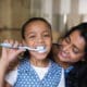 Young girl brushing teeth with mother by her side